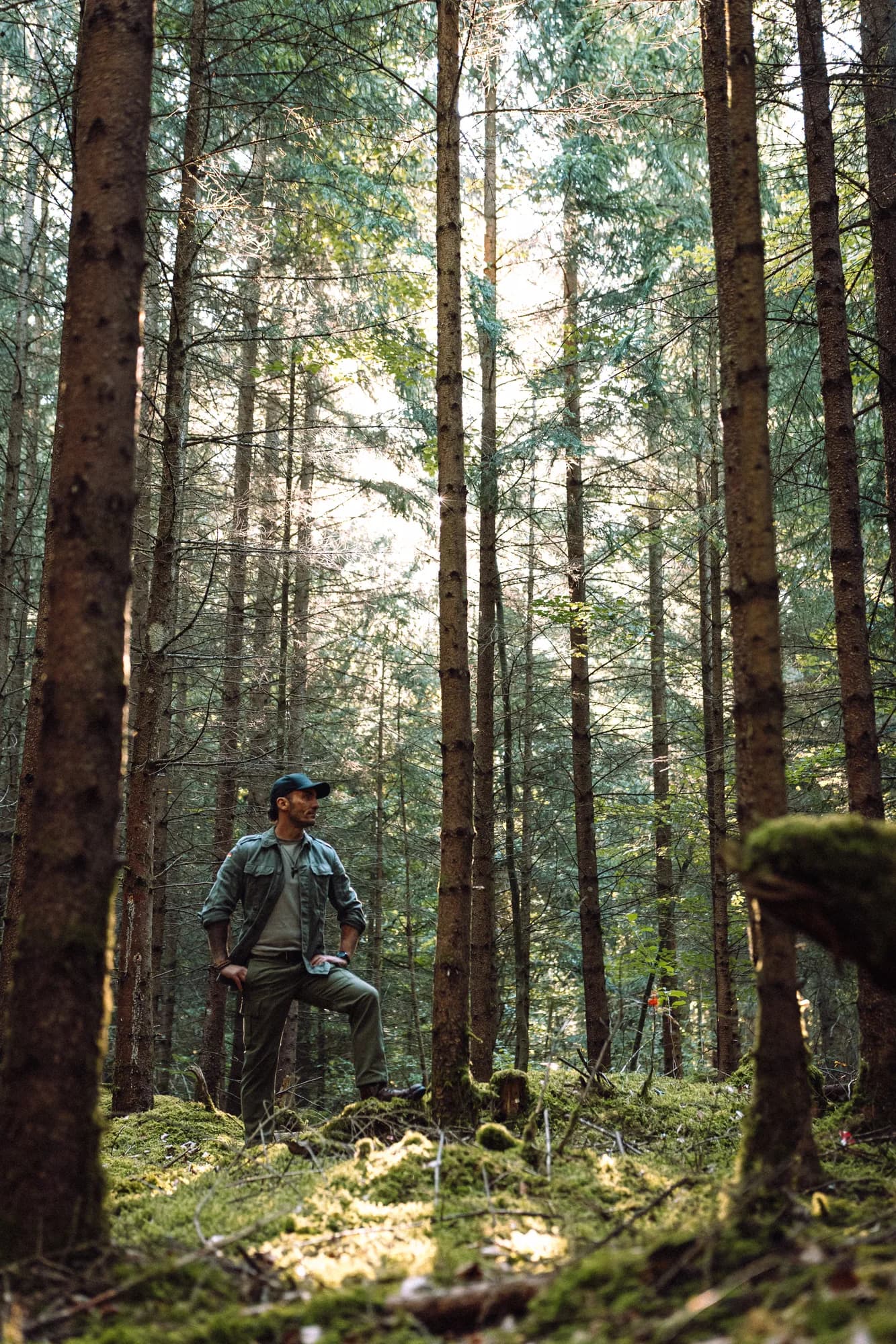 Adrian zwischen hohen Bäumen auf einem moosbewachsenen Waldweg
