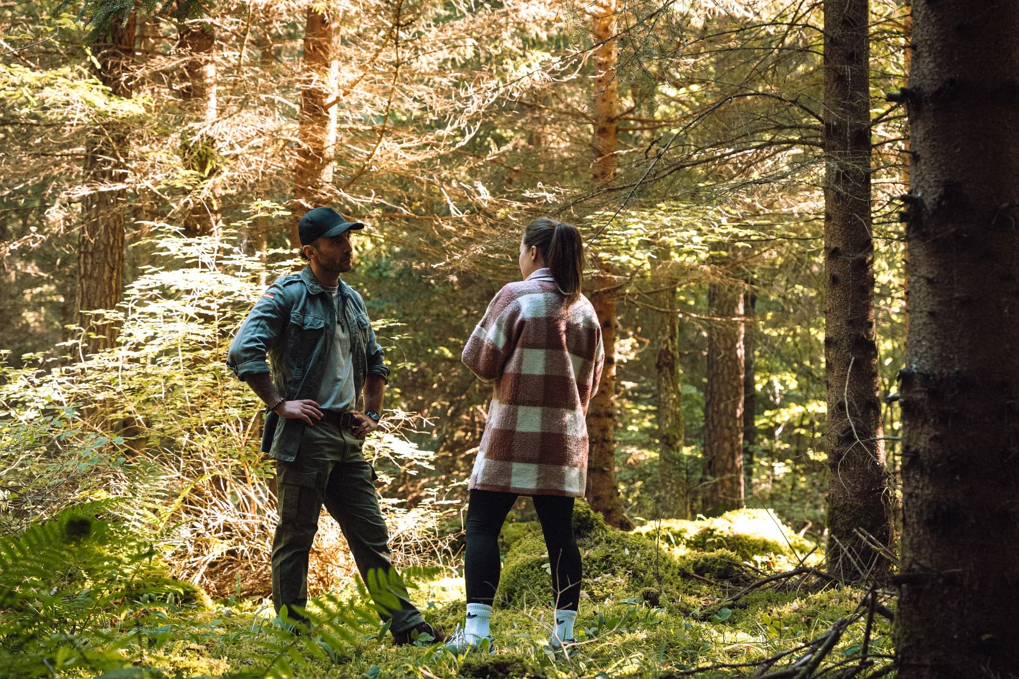 Adrian und eine Gesprächspartnerin stehen sich auf einer Lichtung im Wald gegenüber