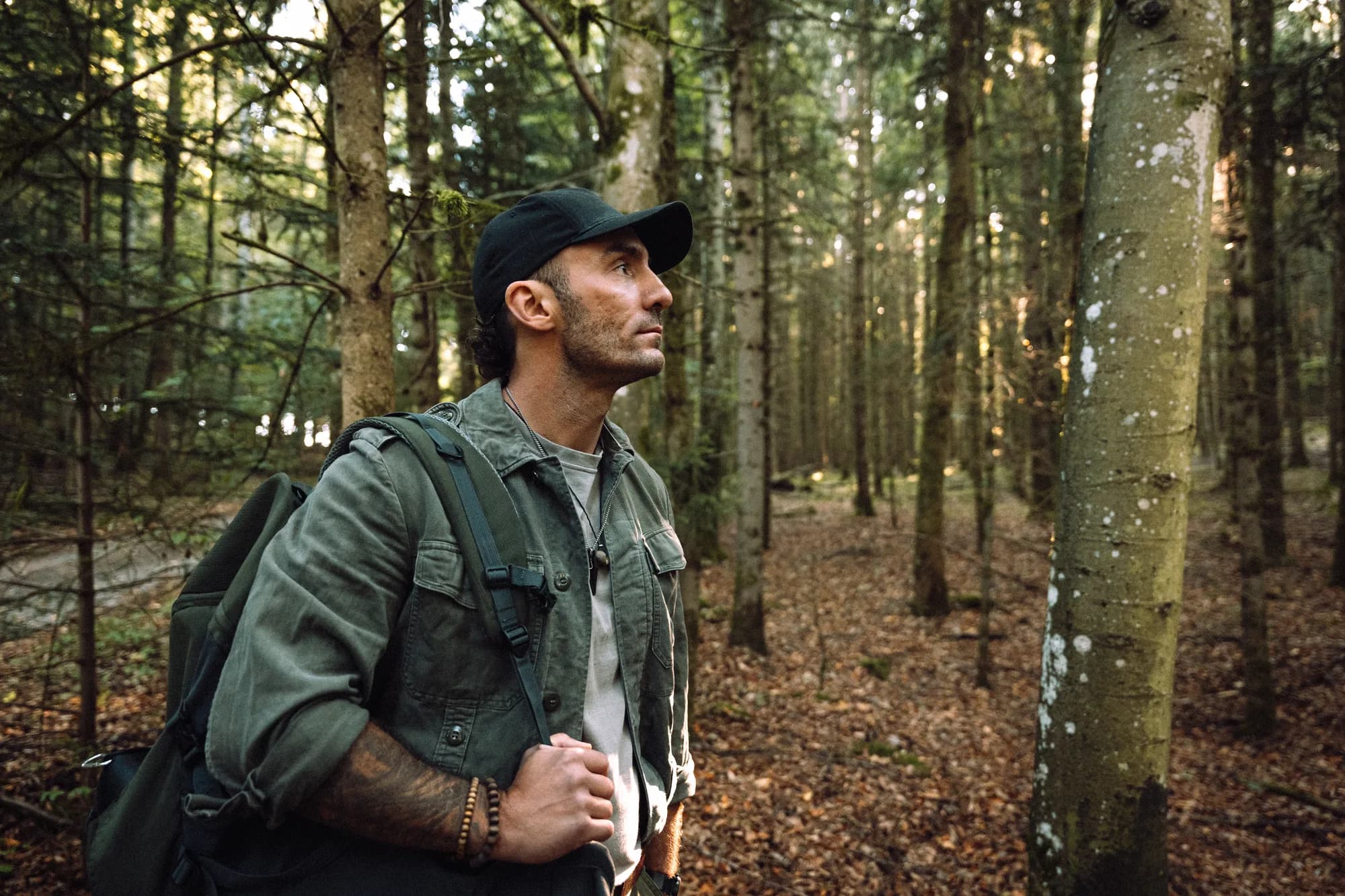 Adrian mit Rucksack im Wald, den Blick in die Baumkronen gerichtet